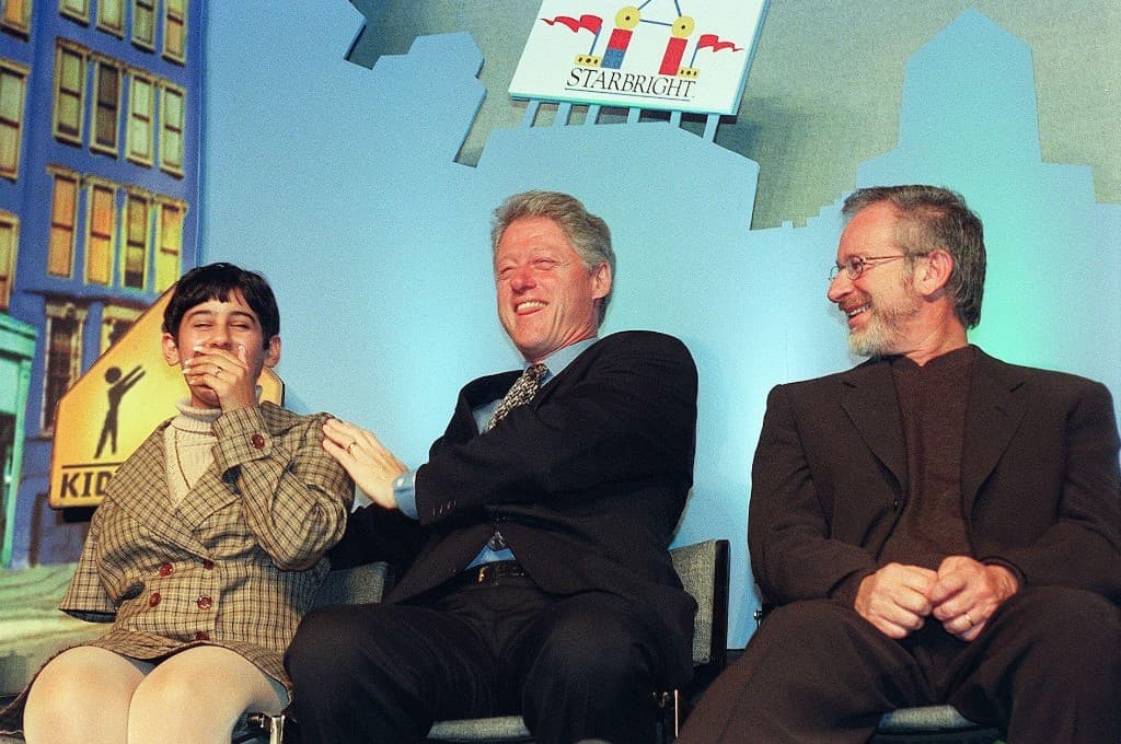 A child seated beside President Bill Clinton and Steven Spielberg at a Starbright Foundation event in 1997